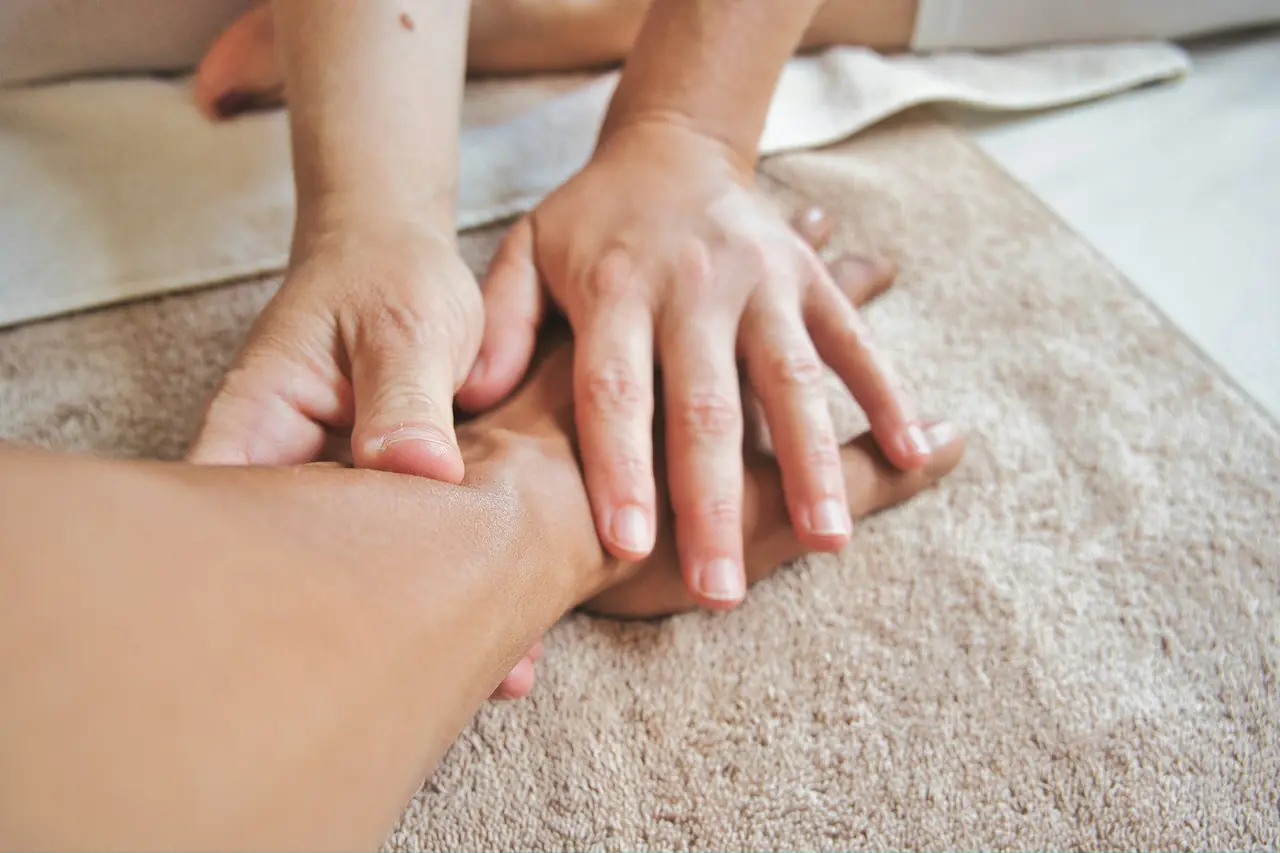 A therapist's hands massage a client's forearm over a soft beige towel.